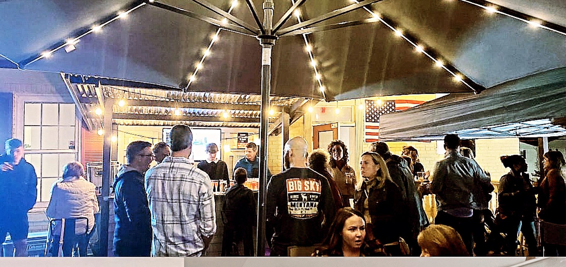 An evening rooftop social at The Hive with guests mingling under market umbrellas and warm string lights